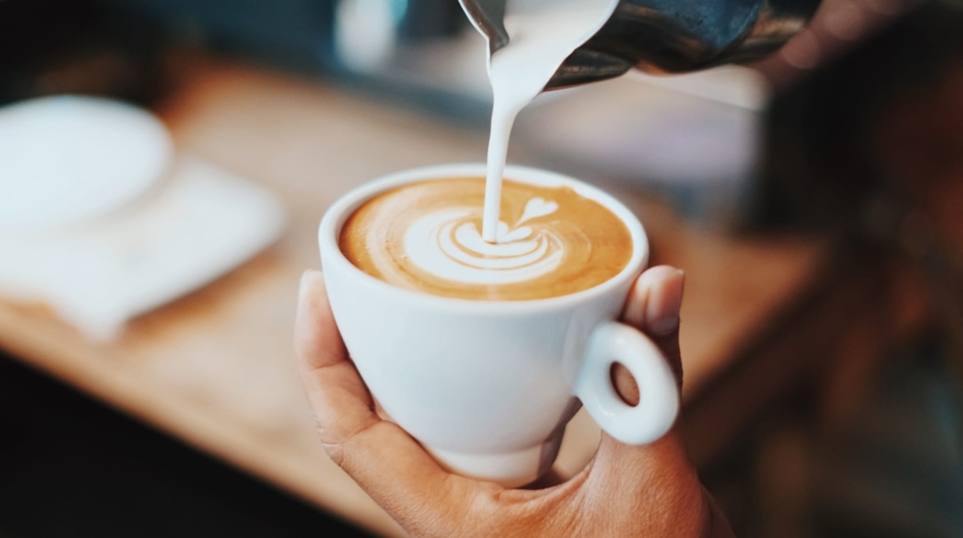 Jemand gießt geschäumte Milch in eine Kaffeetasse und bereitet einen schönen Cappuccino zu